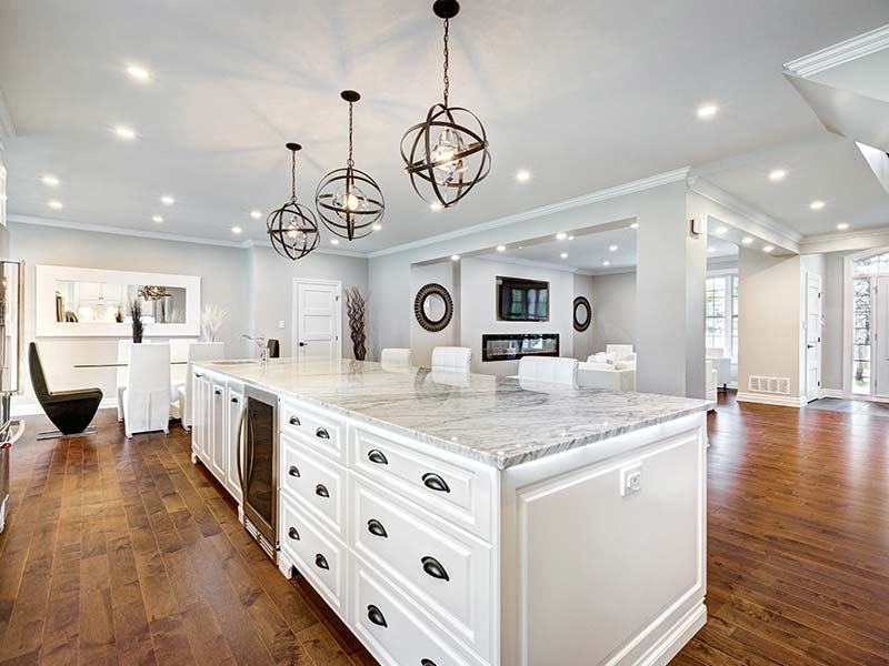 White kitchen with a long island, marble countertop, and pendant lighting